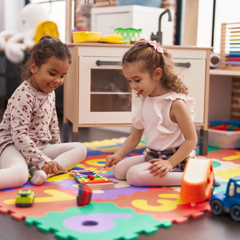 Two,Kids,Playing,Xylophone,Sitting,On,Floor,At,Kindergarten Two kids playing with a xylophone during free play at Building Brilliance Day Care in Long Island City.